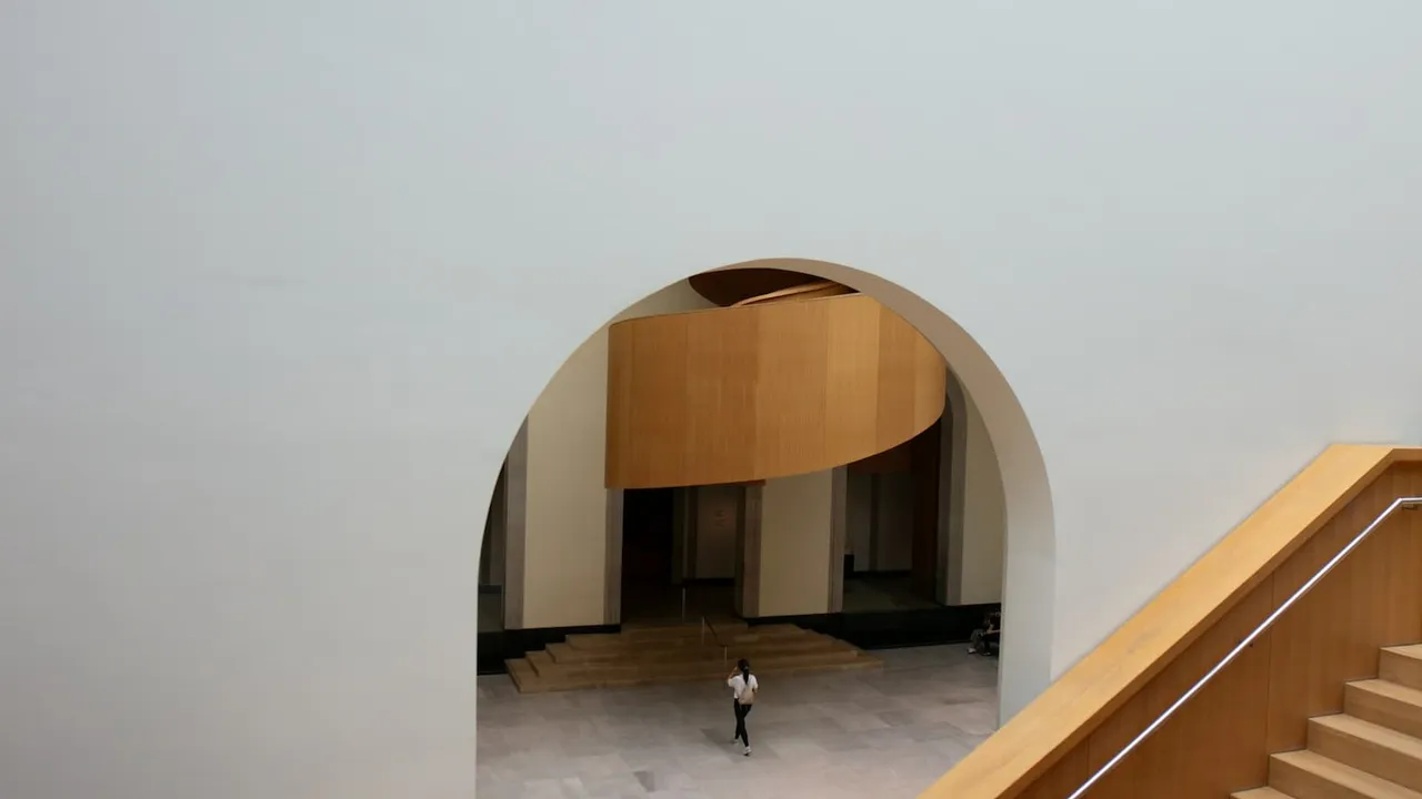 An arch with a person walking towards some stairs.